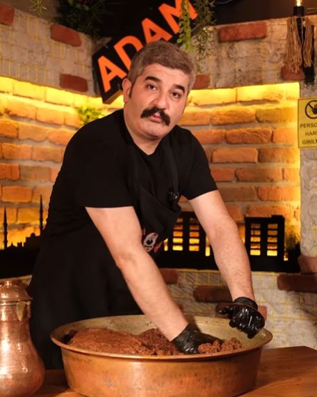 Siyah önlüklü usta, tuğla duvarın ve neon ADAM GİBİ tabelasının önünde bakır tepside çiğ köfte yoğuruyor.